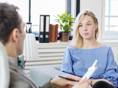 ζωγραφιά που απεικονίζει μια θεραπεύτρια και μια θεραπευόμενη με τη τσάντα της θεραπεύτριας να έχει ανοίξει και να προβάλλει προσωπικά αντικείμενα